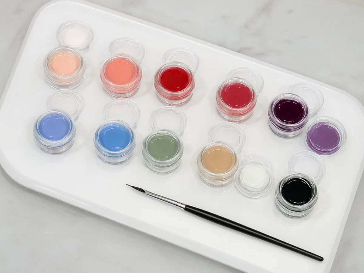 A tray of small glass pots of gel color with a nail art brush